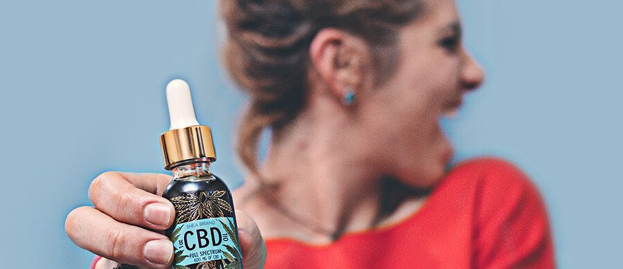 Woman holding out CBD oil with a stretched hand and smiling. How to market CBD products on Google and Facebook. How to promote CBD products on Facebook. Advertise CDB on Google PPC.