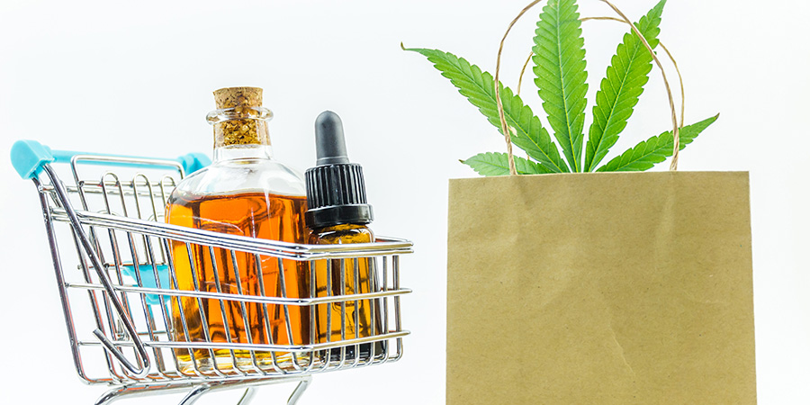 cannabis oil, THC oil, and CBD oil in a shopping cart next to a cannabis leaf in a paper bag. Marketing cannabis dispensary